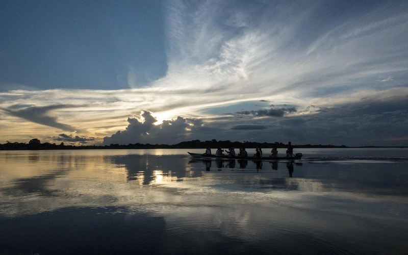 Wooden pier extending over a calm lake at sunset, with the sun reflecting on the water and soft clouds in the sky, creating a peaceful golden scene.